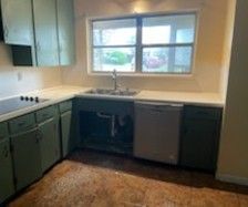 A kitchen with a sink , stove , dishwasher and window.