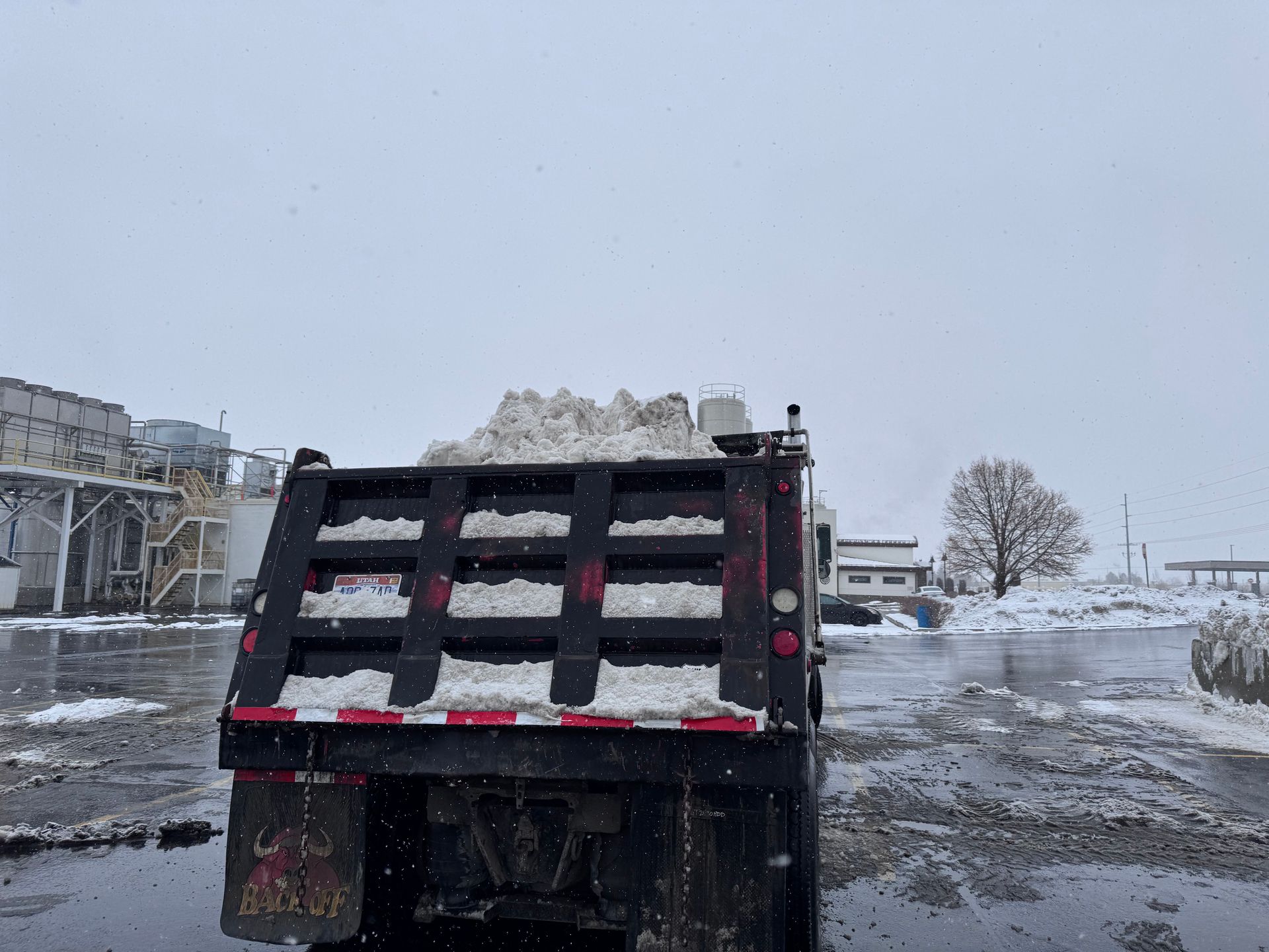 Snow-filled dump truck on a snowy day. Industrial setting with buildings in the background.