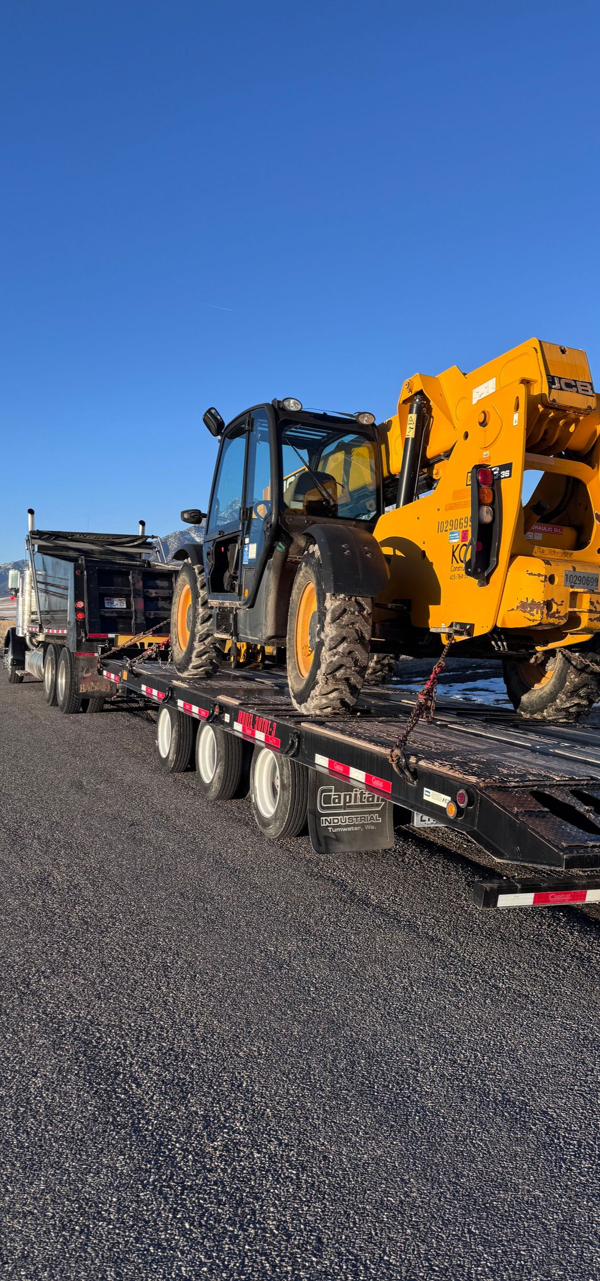 A yellow construction vehicle loaded on a black flatbed trailer, under a clear, blue sky.