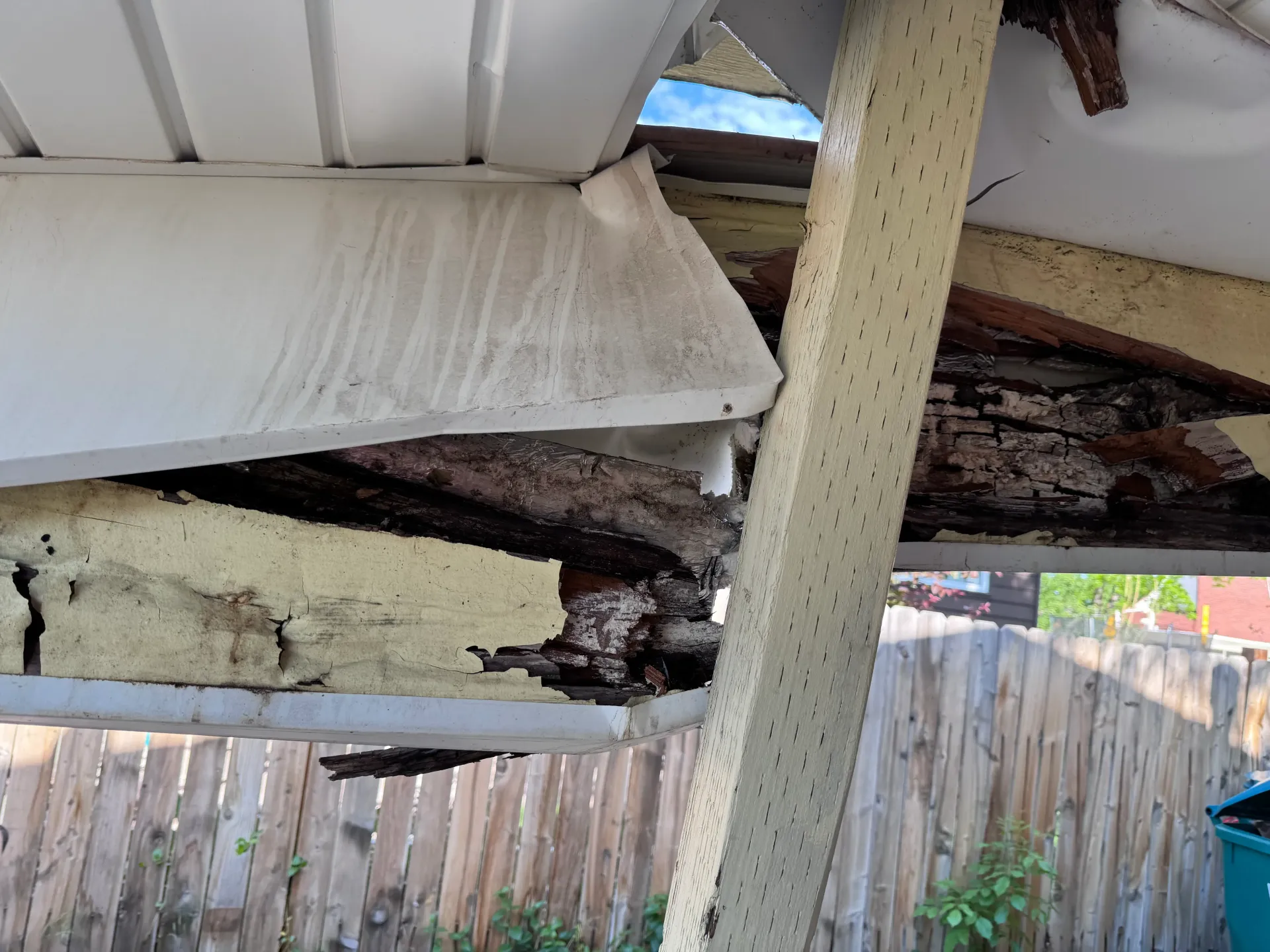 Damaged wooden structure of a porch roof, showing rot and collapsed sections.