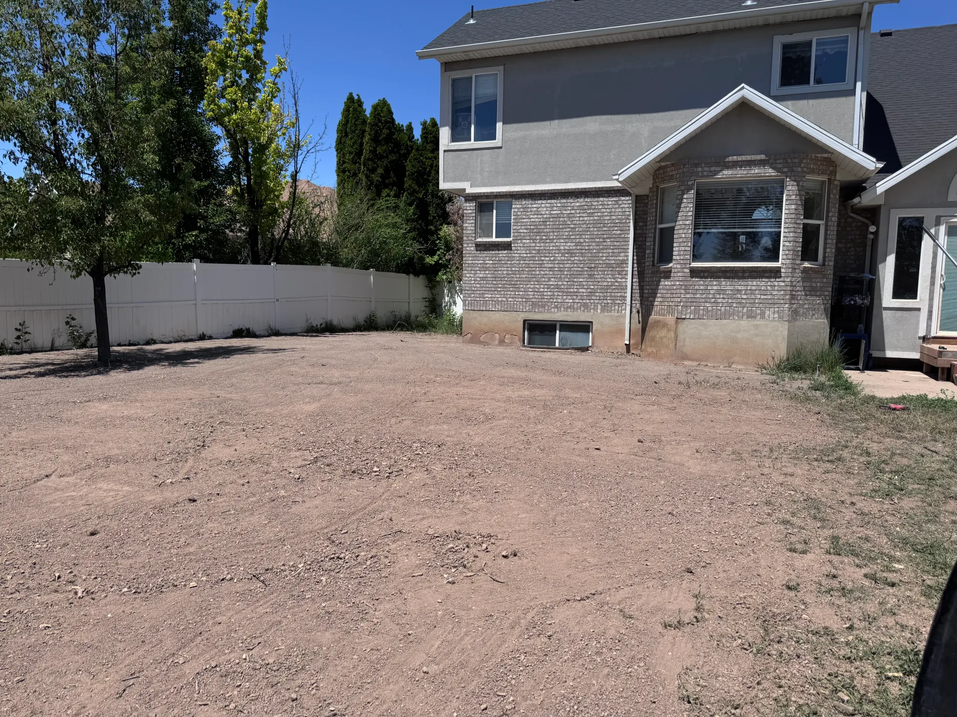 Backyard with gravel ground in front of a house with stone and gray siding.