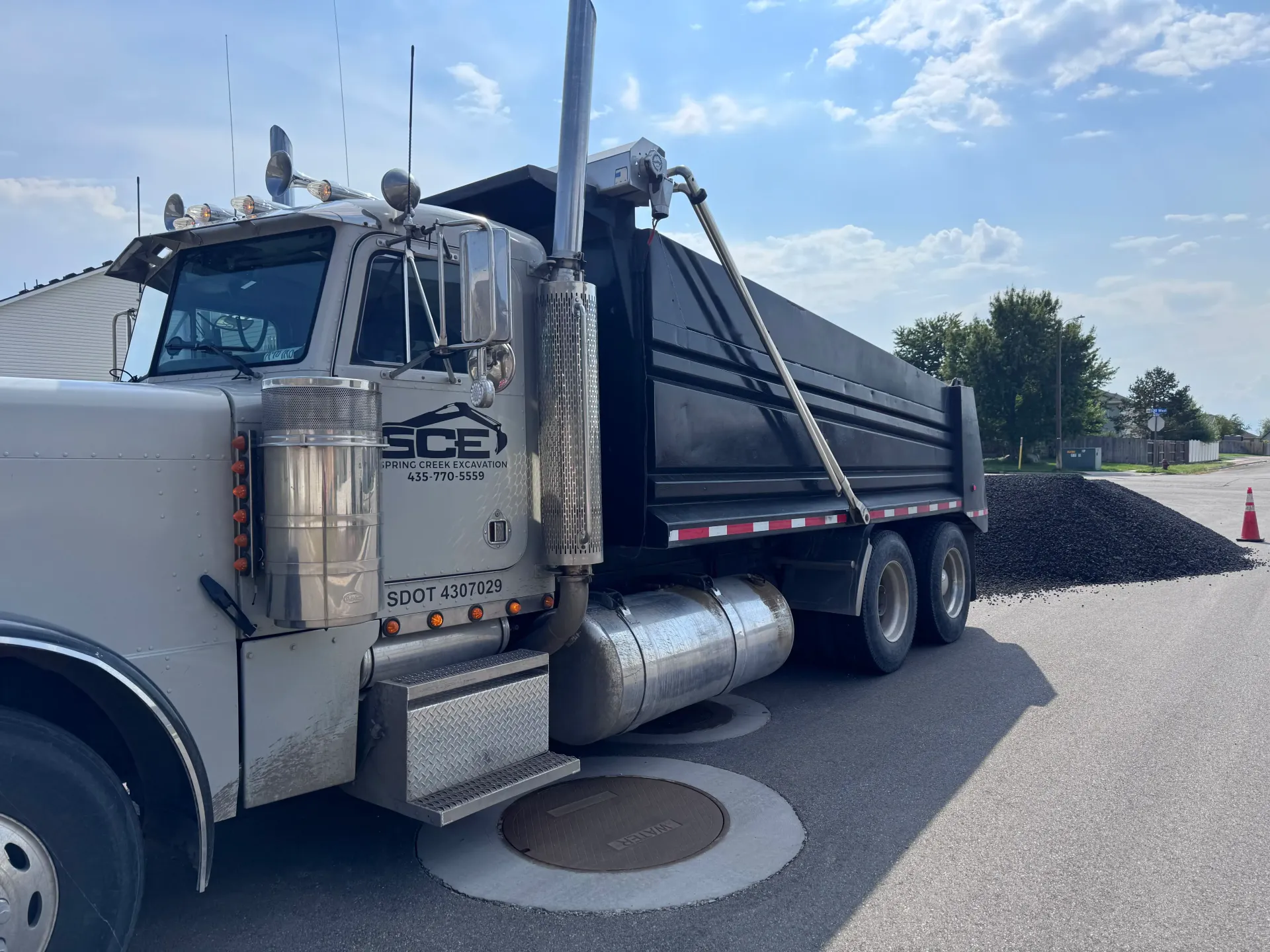 Dump truck unloading asphalt on a paved road under a partly cloudy sky.