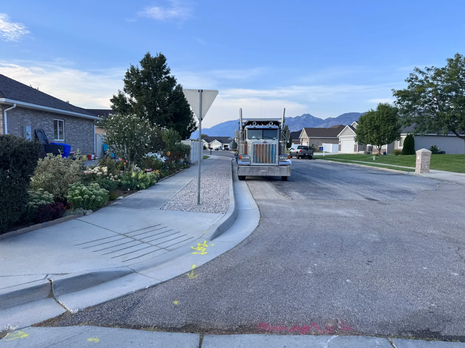 Truck on a road, gravel being poured, residential neighborhood, blue sky, mountains in the distance.
