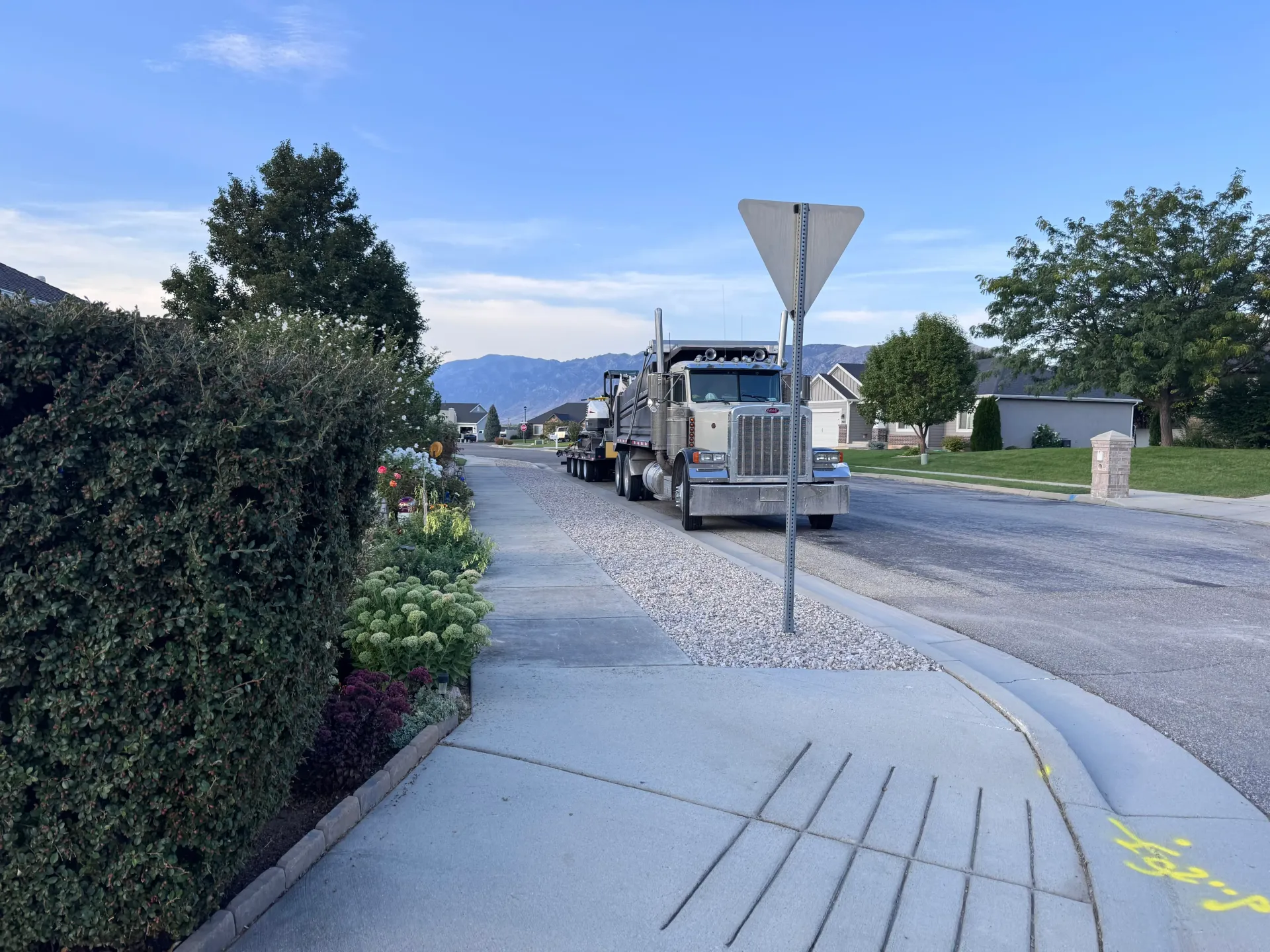 Truck on gravel road near residential area. A yield sign is in the foreground.