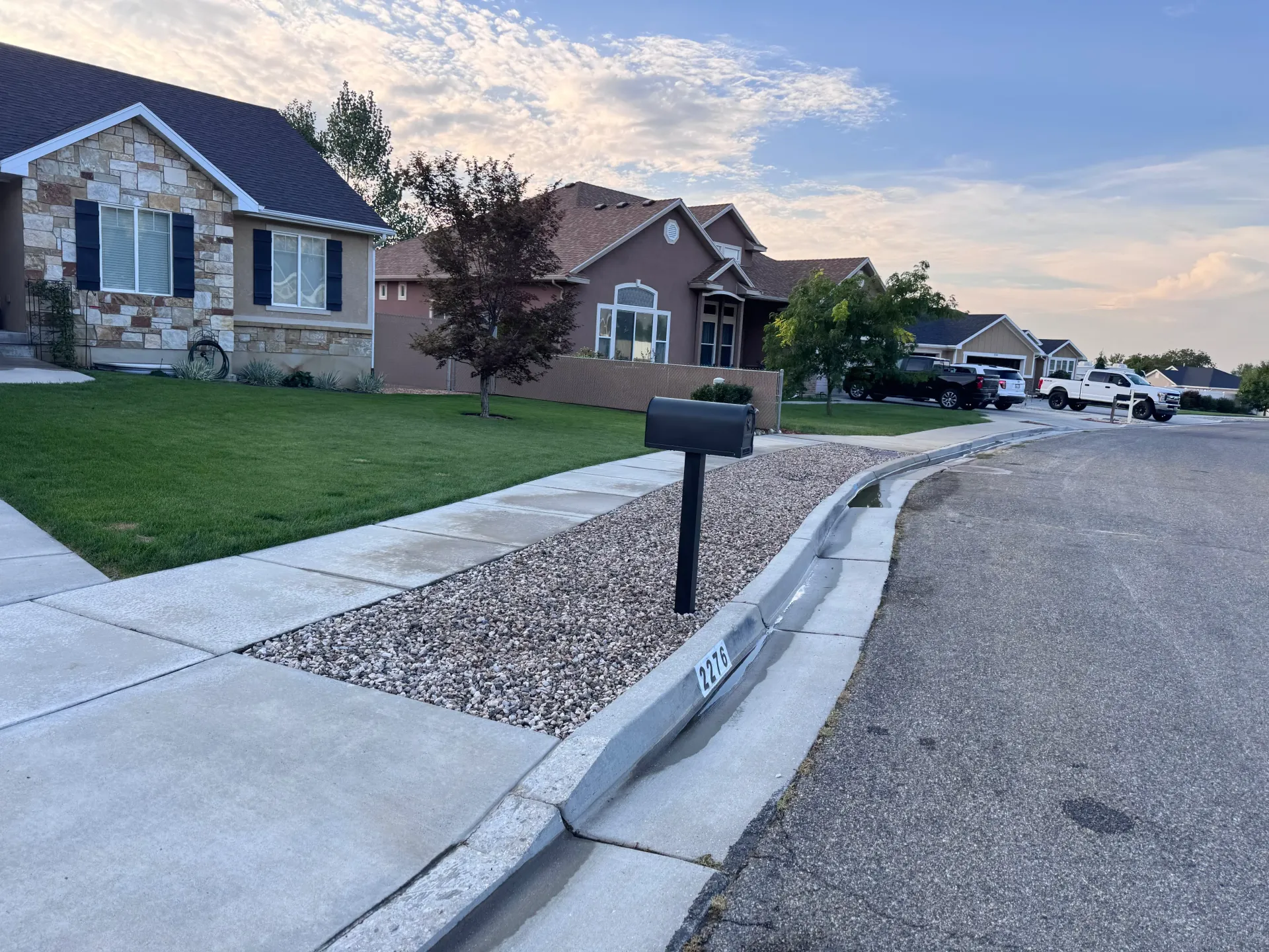 Residential street with houses, sidewalks, and mailbox in a rock-filled median strip.
