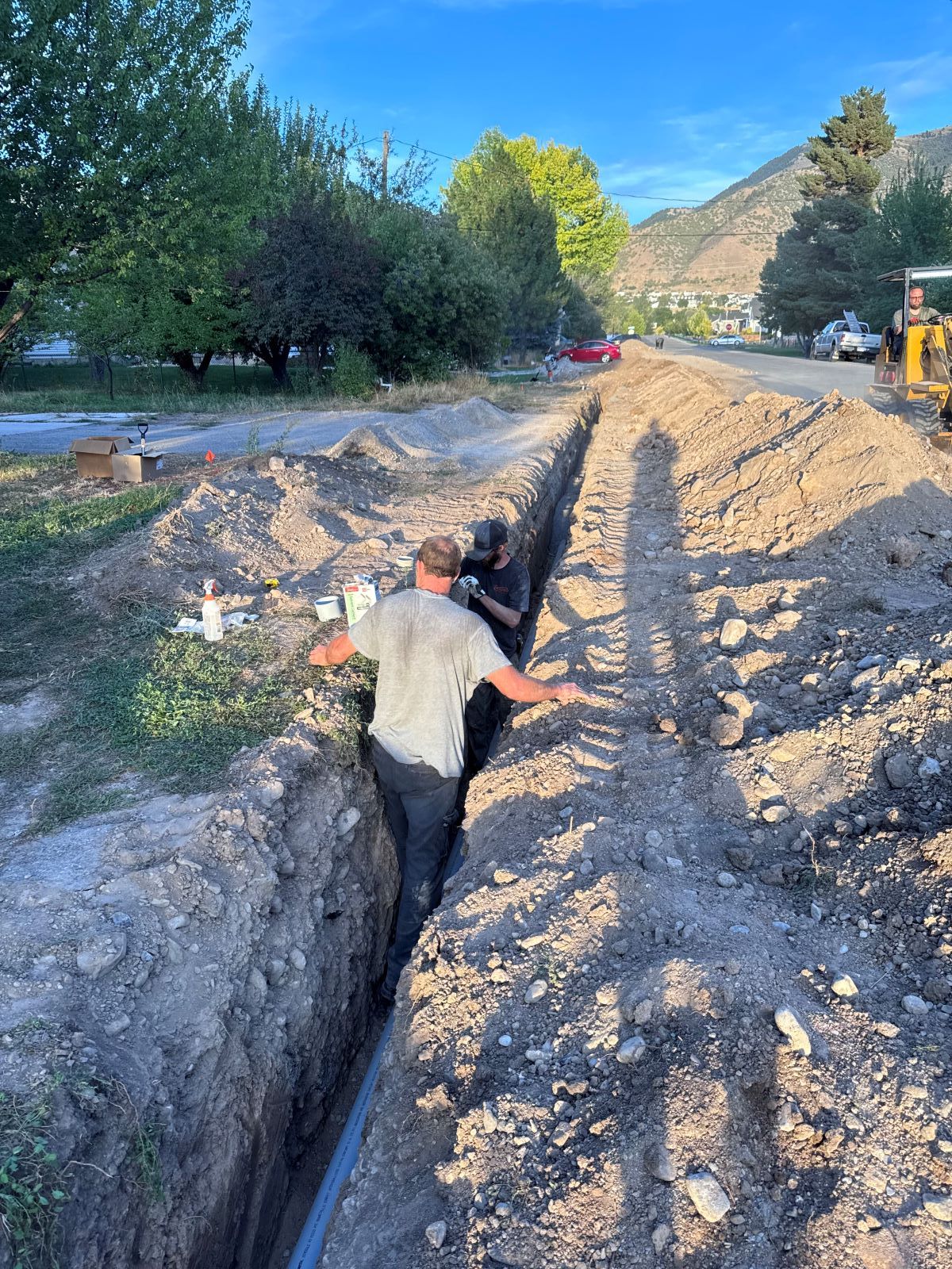 Two workers in a trench installing pipe outdoors, sunny day.