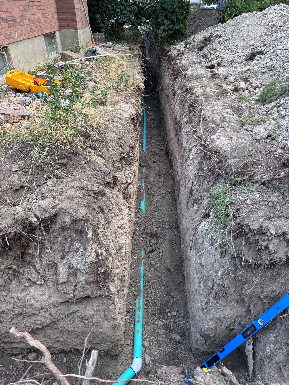 Trench dug with blue pipes installed, near a brick building.