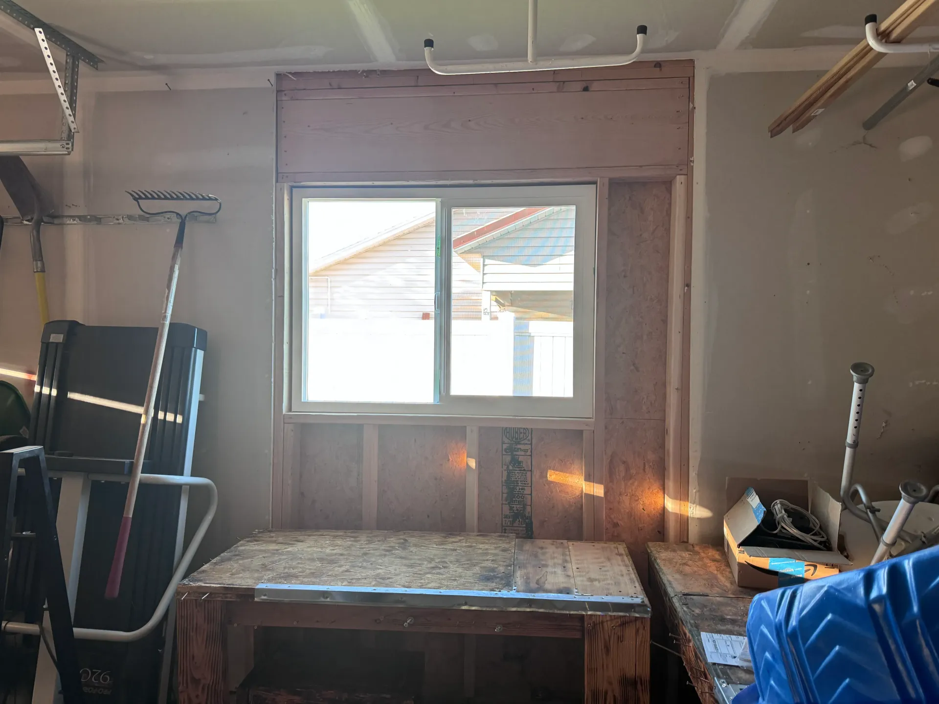 Garage interior with a window, workbench, tools, and exposed wooden framing.