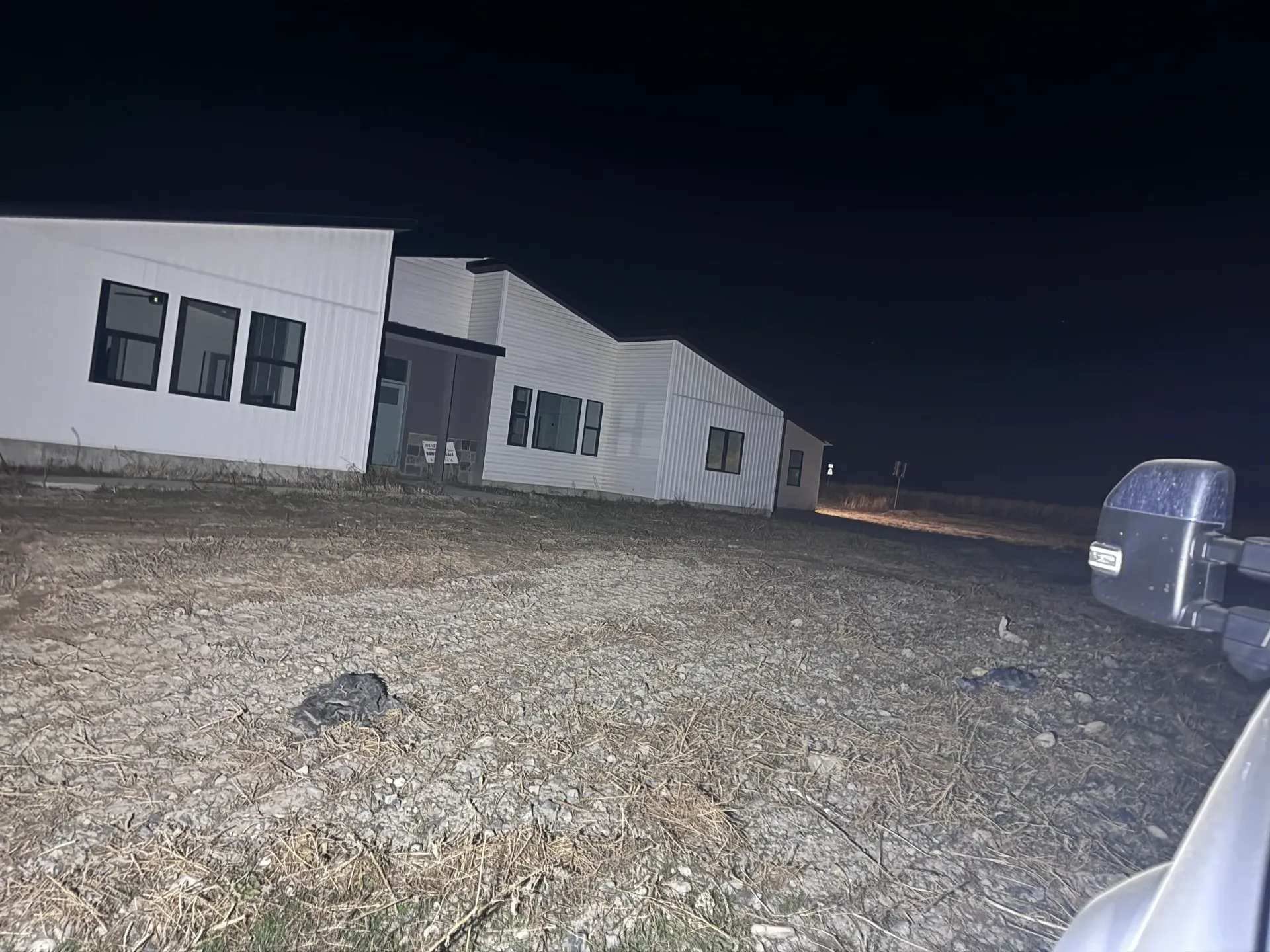 Building at night with illuminated windows, on a gravel lot; dark sky.