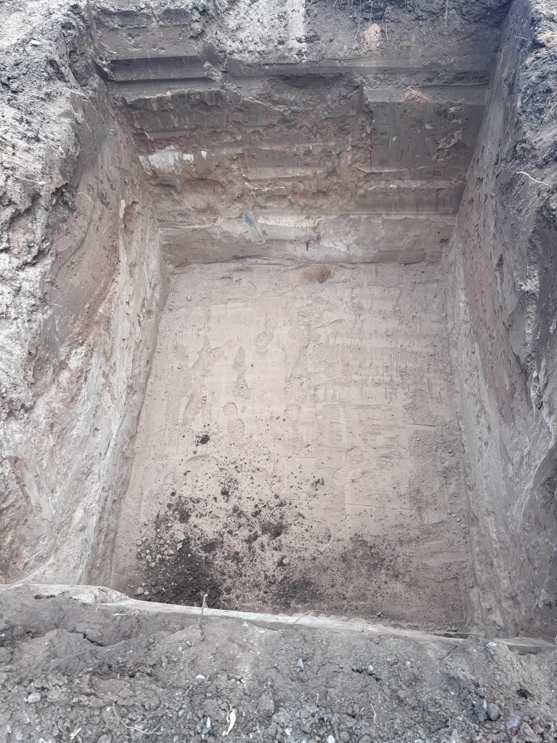 Square excavation pit in earth, showing layered soil, open at top.