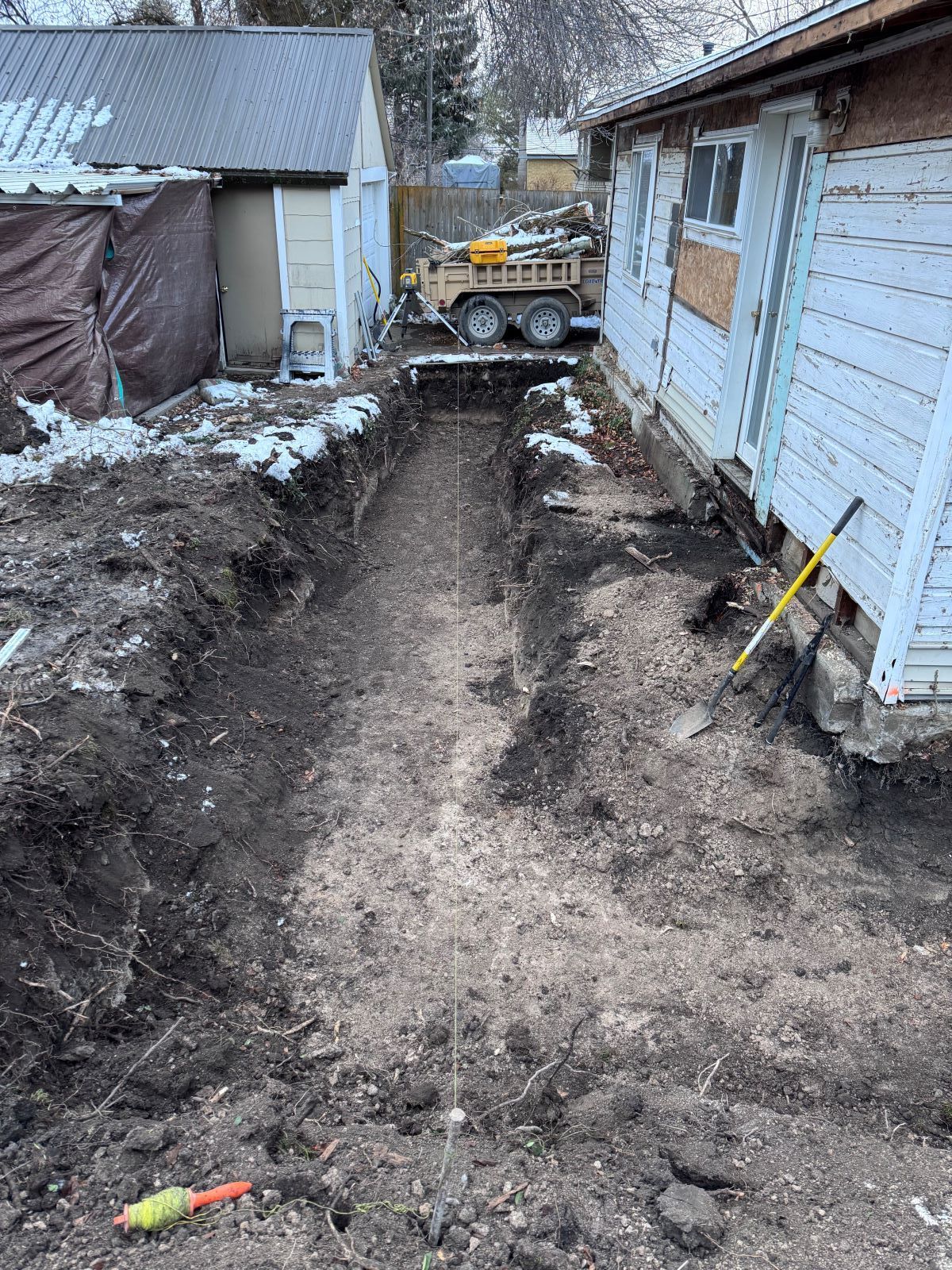 Narrow trench dug beside a house, string stretched along the bottom.