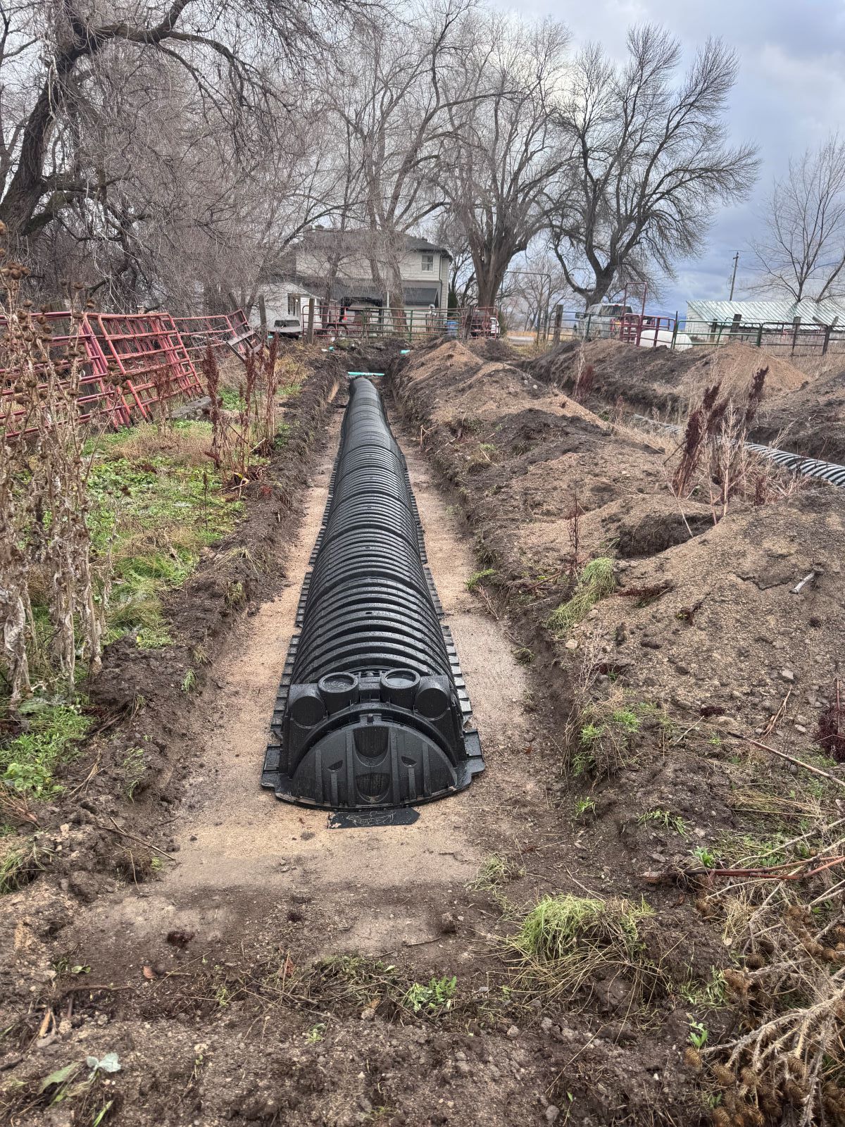 Black drainage structure in a trench, prepared for installation in a yard with a house in the background.