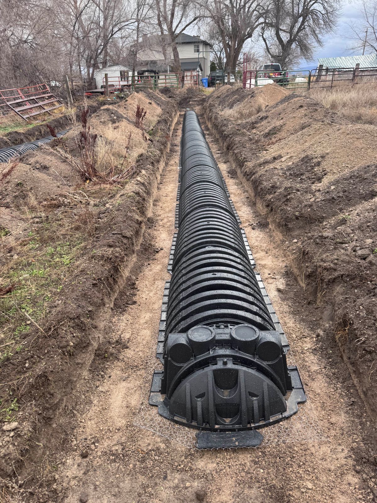 Black plastic drainage system installed in a long trench in a yard, leading toward a house.