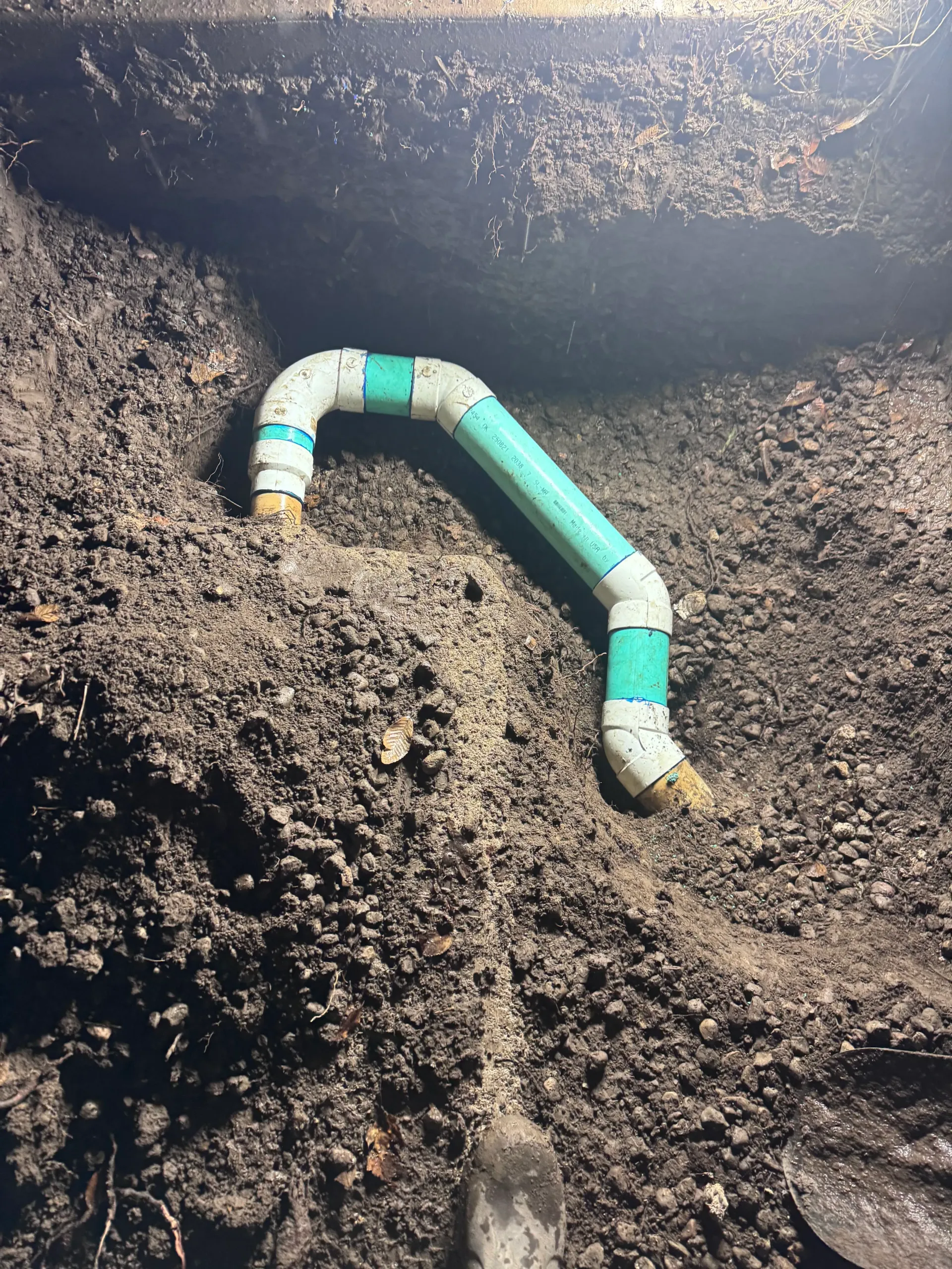 PVC pipe with green tape and white fittings in dark soil.