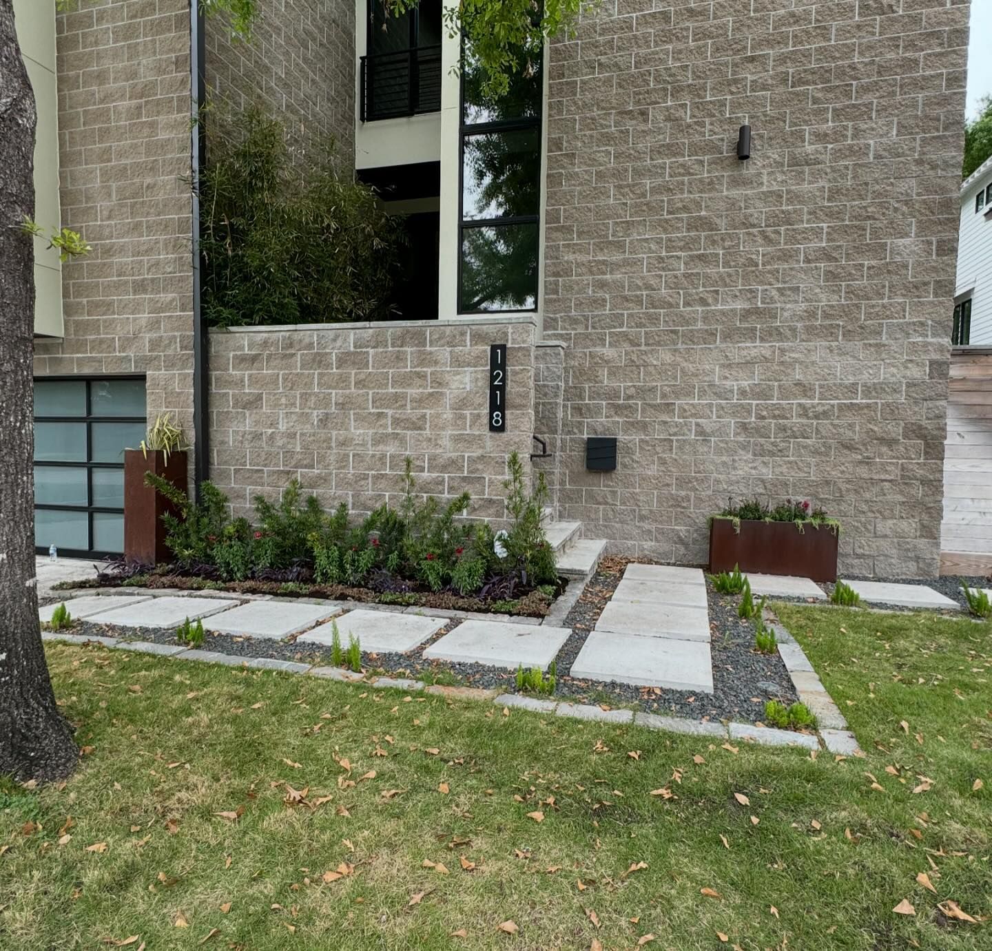 Exterior view of a modern house with stone facade, square walkway, and landscaped yard.
