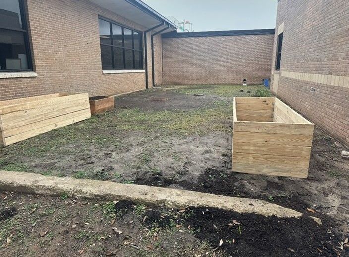 A courtyard with bare soil, two wooden planters, and brick walls.
