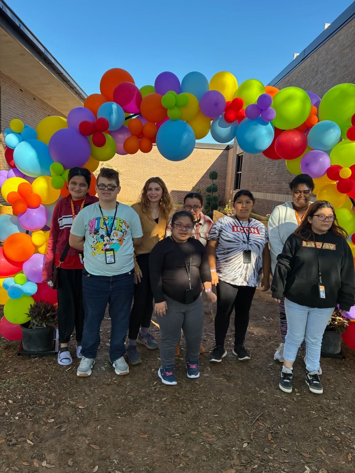 Group of people posing under a colorful balloon arch outside a building.