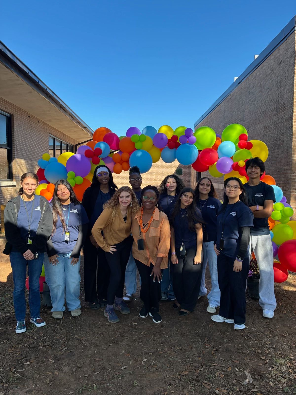 Group of people standing in front of a colorful balloon arch outside a building.