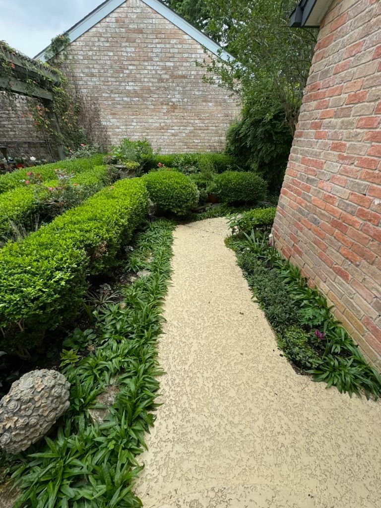 Gravel path winds through a garden flanked by green hedges and brick walls.
