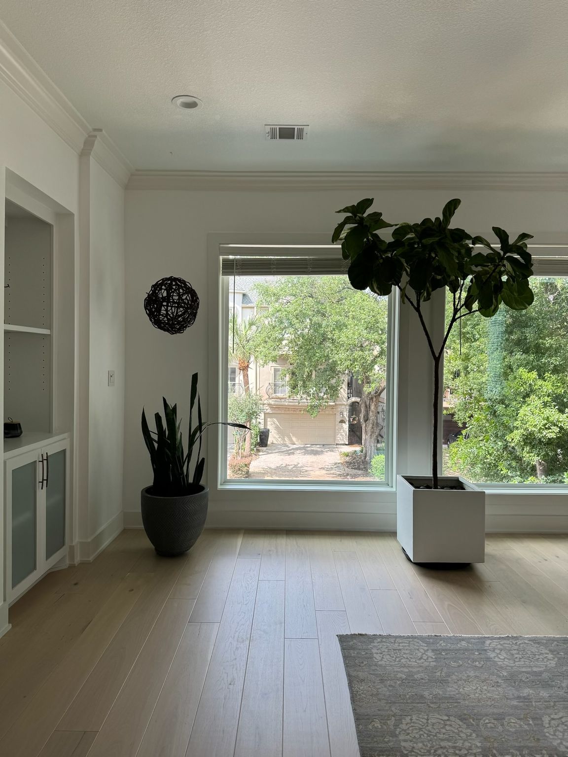 Bright living room with plants by a large window overlooking a yard; hardwood floors.