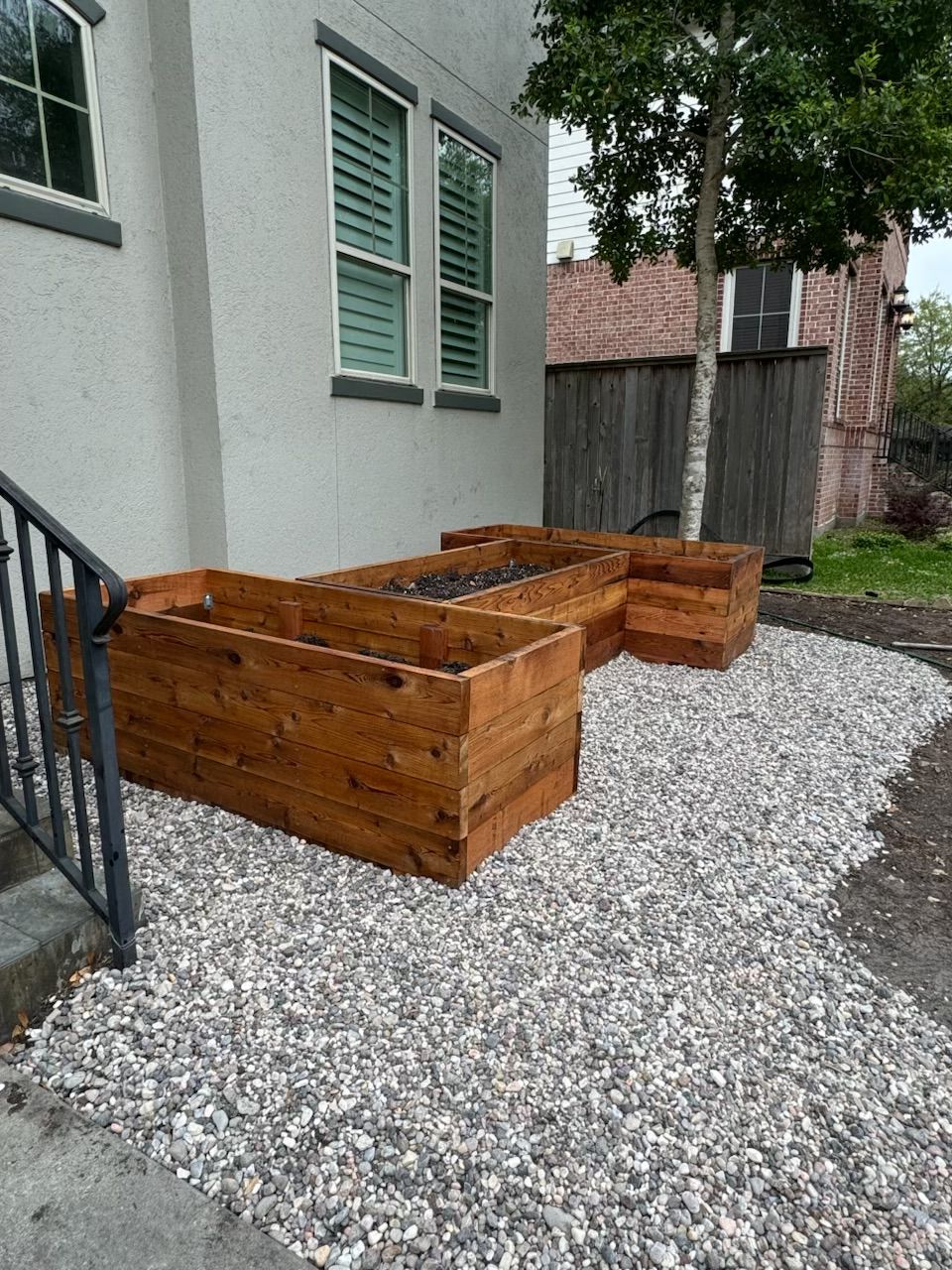 Wooden planters on gravel beside a building with stairs.