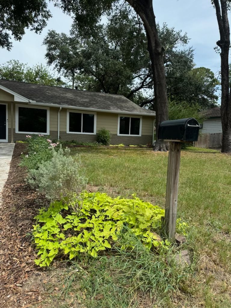 A house with a beige exterior, a lawn, and a mailbox. Yellow-green groundcover in front of the mailbox.