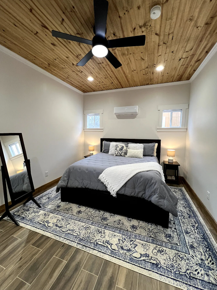 A bedroom with a bed , ceiling fan , mirror and rug.