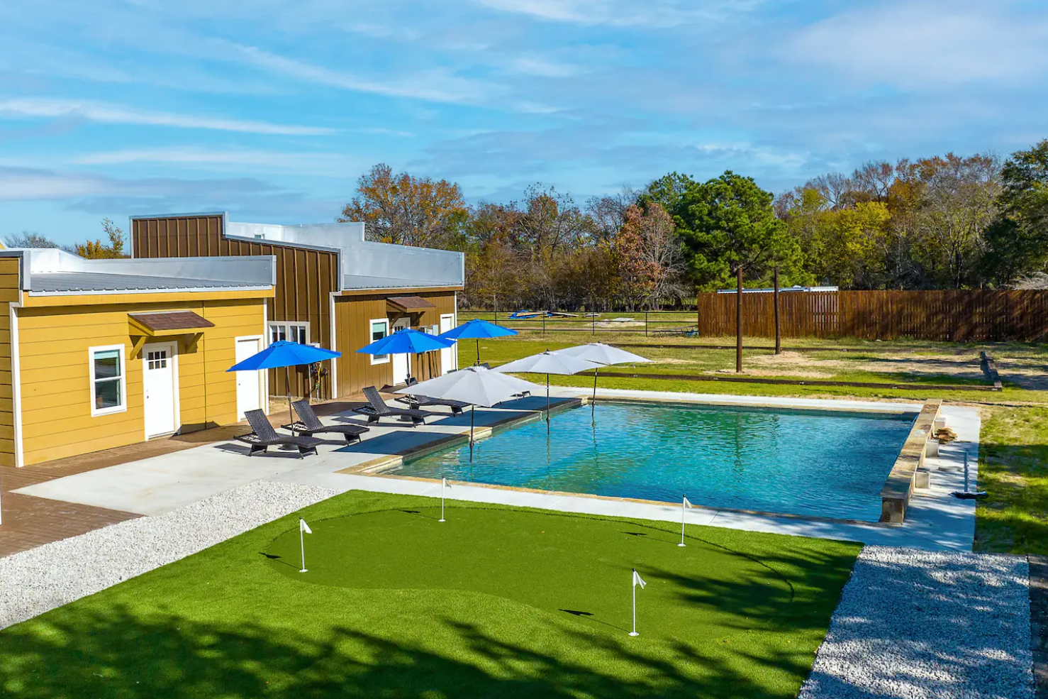 A large swimming pool with umbrellas and chairs in front of a house.