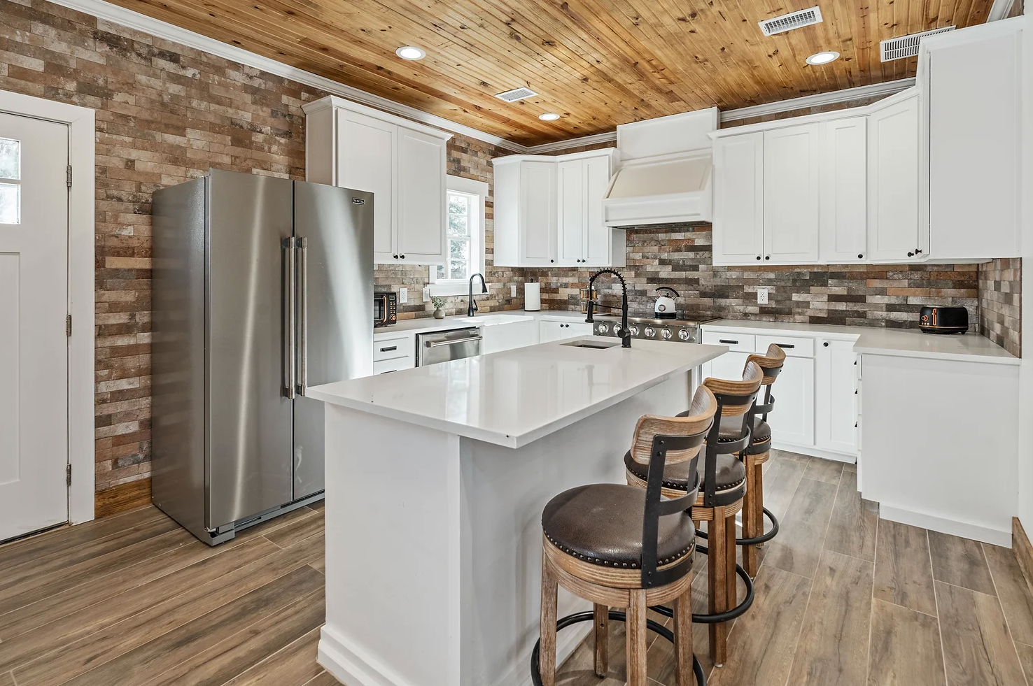 A kitchen with white cabinets , stainless steel appliances , a refrigerator and a large island.
