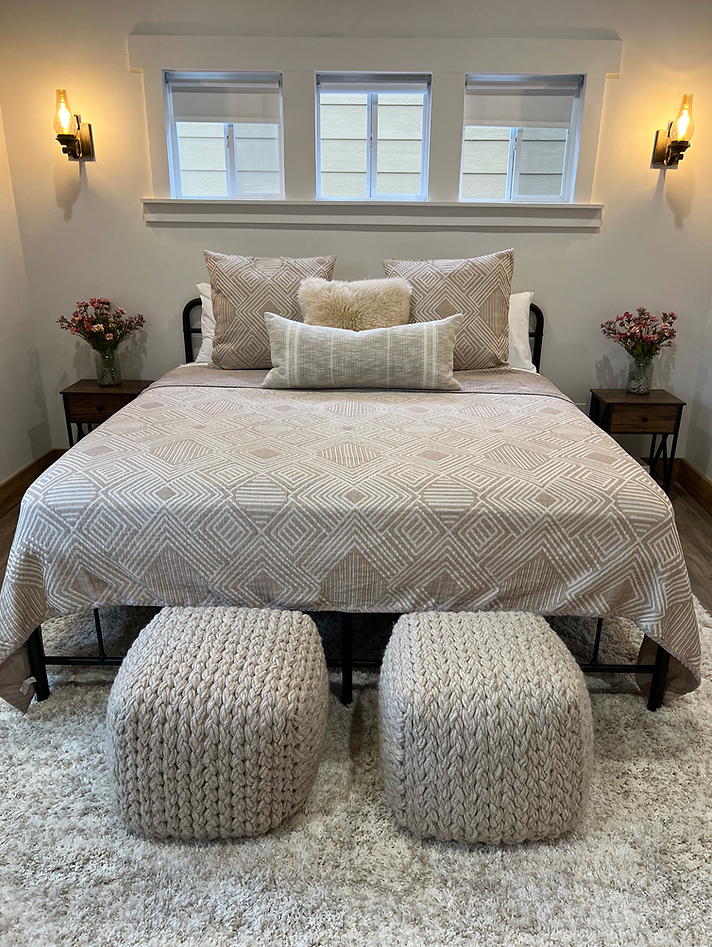 A bedroom with a bed , two ottomans and two windows.
