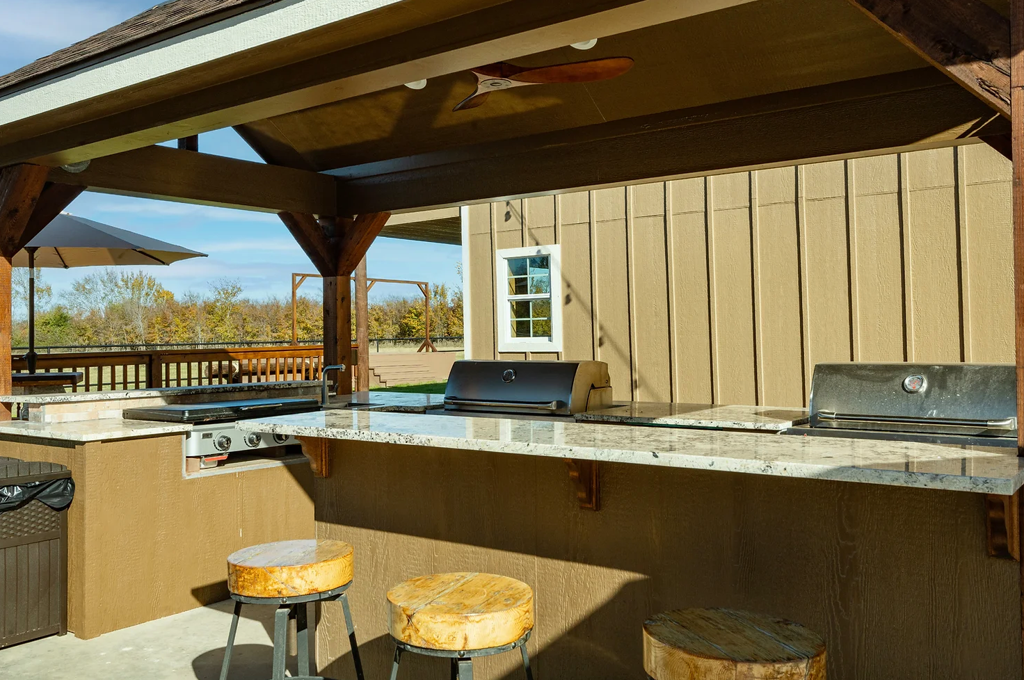 An outdoor kitchen with a grill and stools under a gazebo.