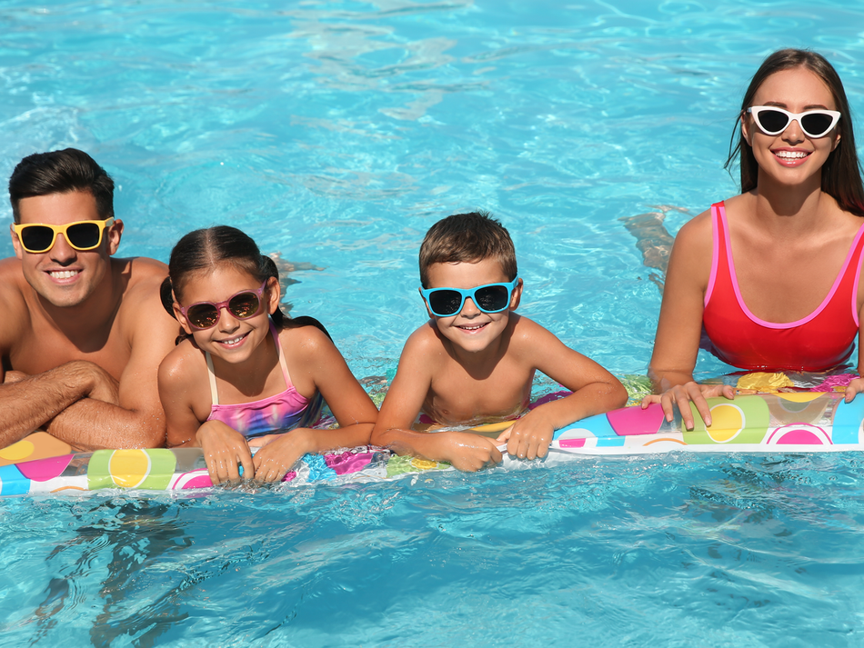 Four people wearing sunglasses smile while relaxing in a swimming pool behind a colorful pool float.