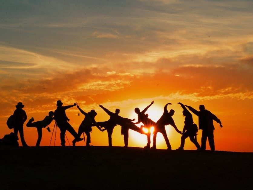 A line of people in silhouette posing playfully against a vibrant, golden sunset.