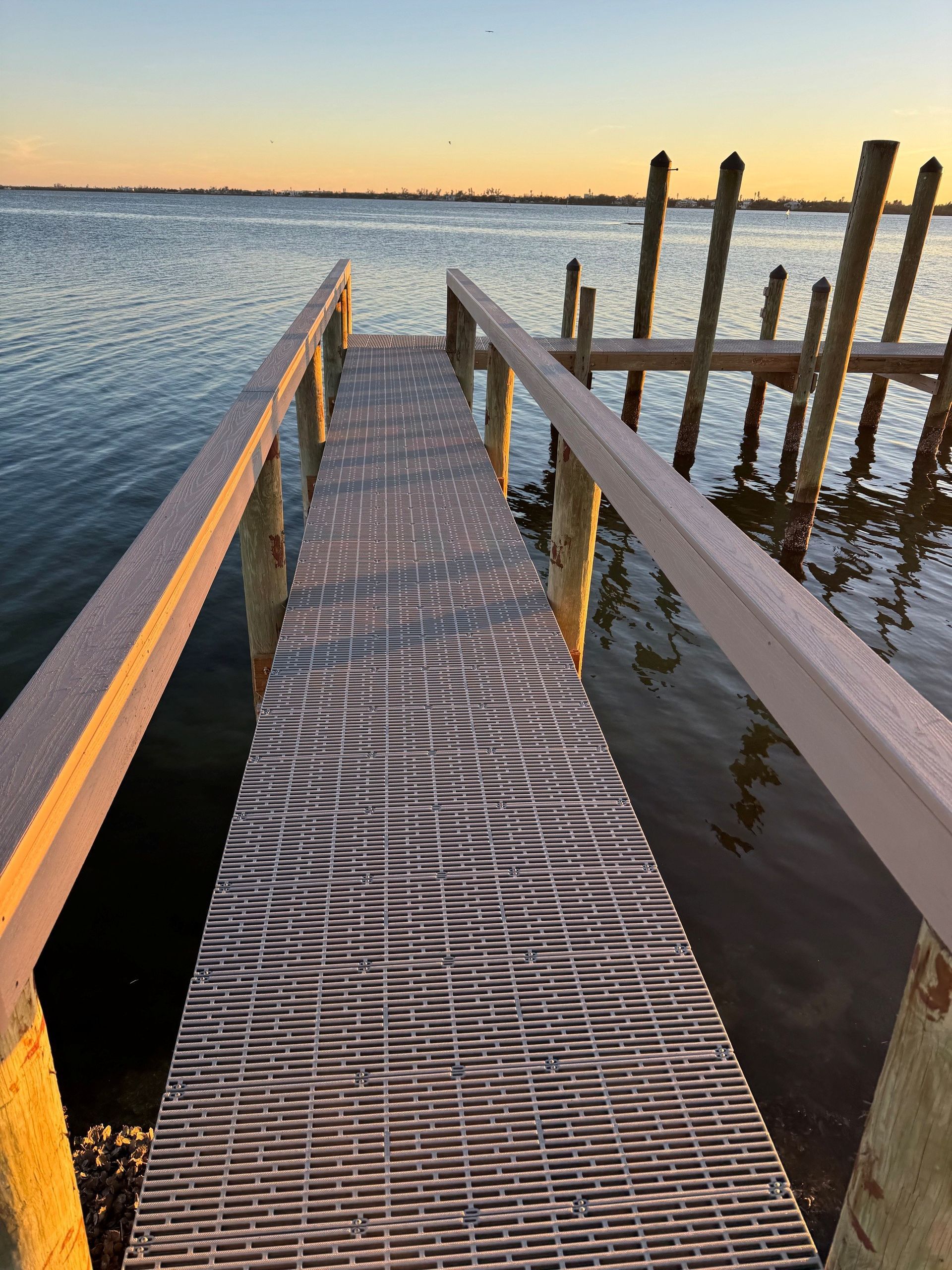 Wooden dock at sunset over calm water, with weathered posts and a netted walkway.