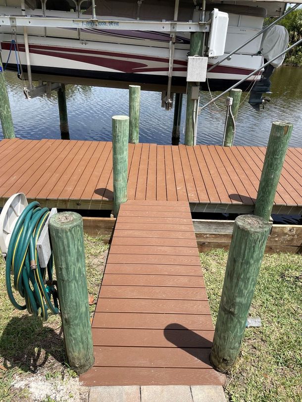 Wooden dock with a hose reel on the left, leading to a marina with boats on calm water.