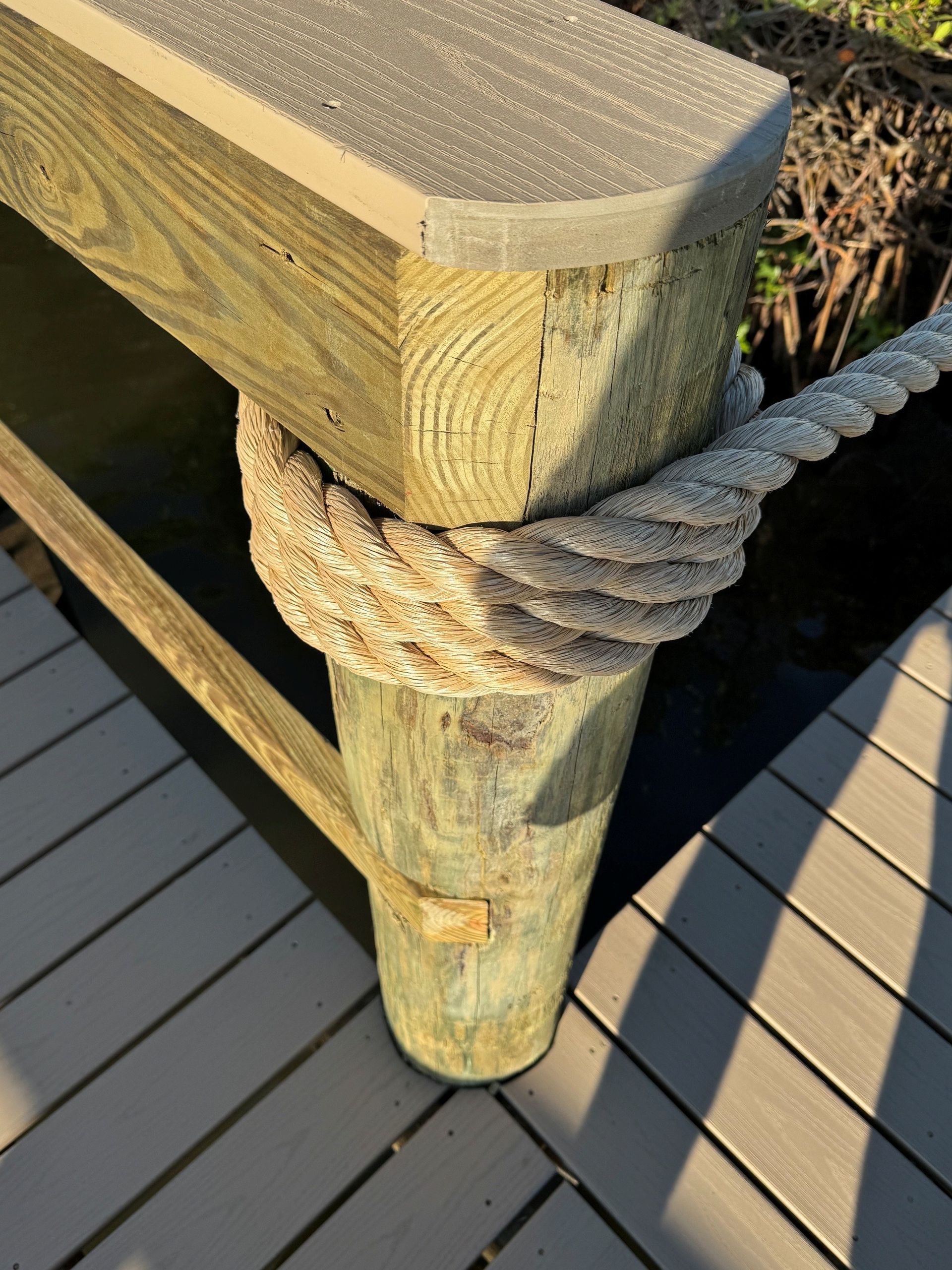 Wooden dock railing post wrapped with thick rope beside a gray deck.