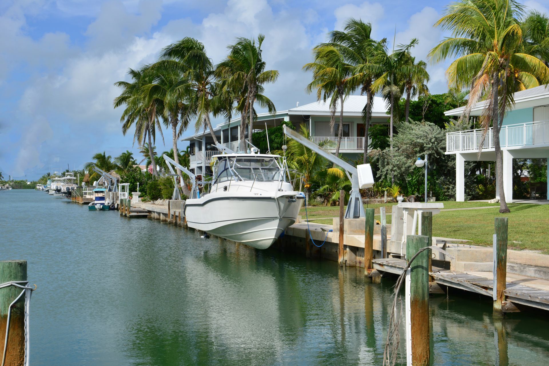 White boat docked along a calm canal beside palm trees and waterfront homes on a sunny day