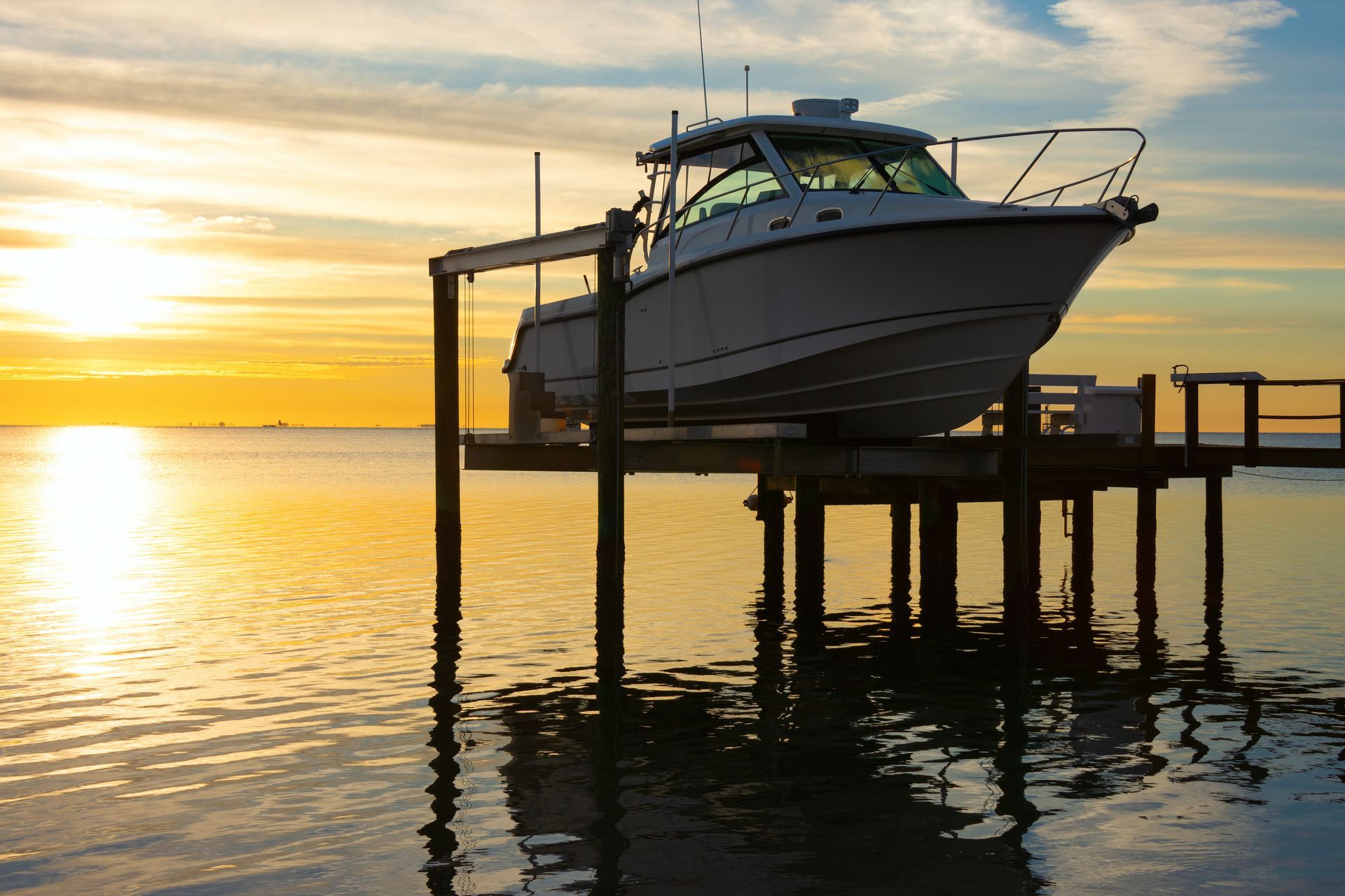 Boat on a lift at sunset over calm water, with golden sky reflections.