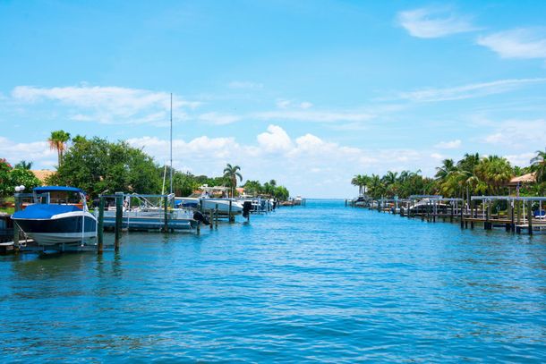 Sunny marina canal with boats, docks, and palm trees under a blue sky