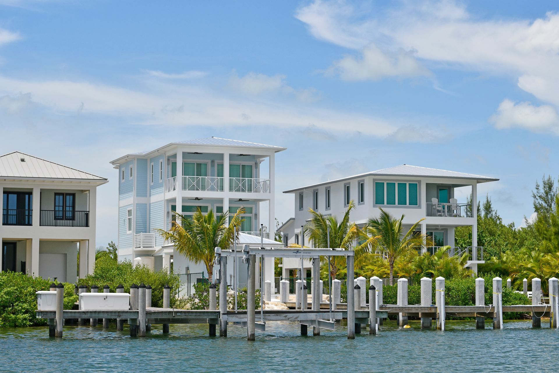 Modern waterfront homes with docks and palm trees under a blue sky