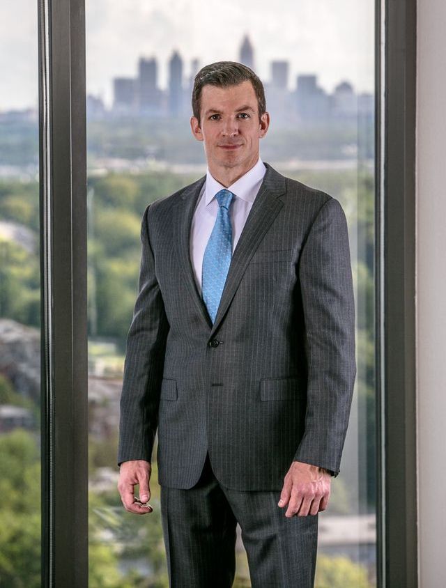 A man in a suit and tie is standing in front of a window.