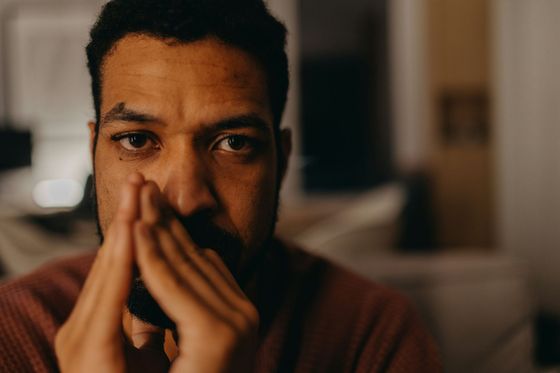 A man with a beard is covering his mouth with his hands.