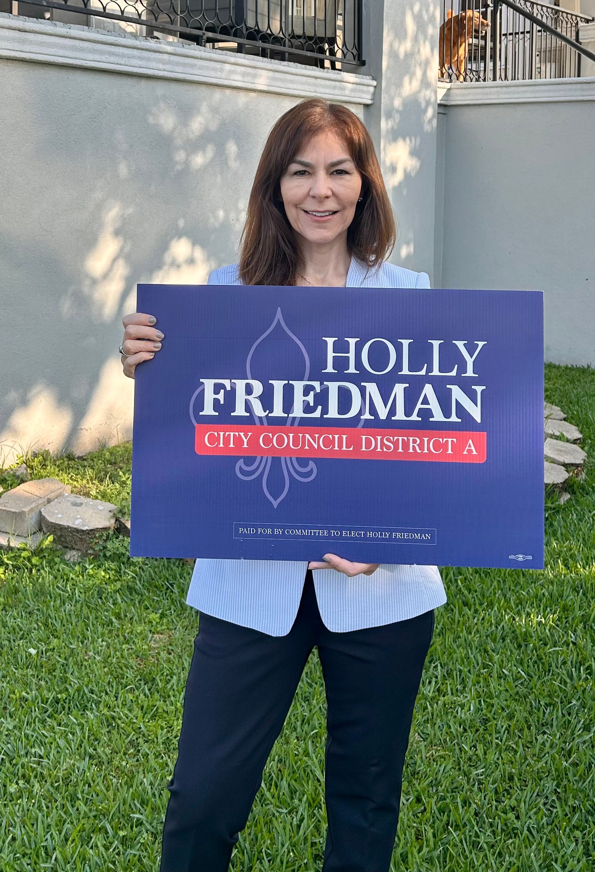 Holly is holding a Holly Friedman sign in front of a house.