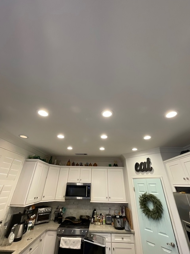 A kitchen with white cabinets , a stove , a microwave , and a wreath on the door.