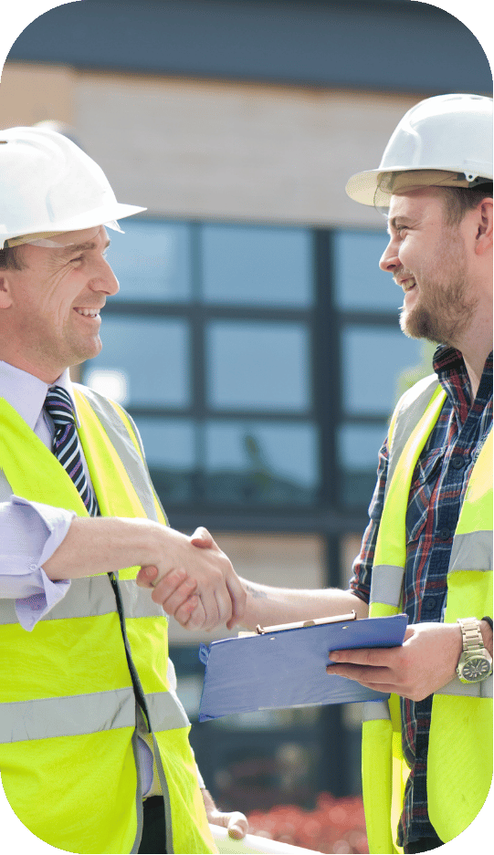 Two construction workers are shaking hands in front of a building.