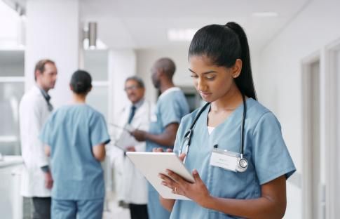 A nurse is looking at a tablet in a hospital hallway.