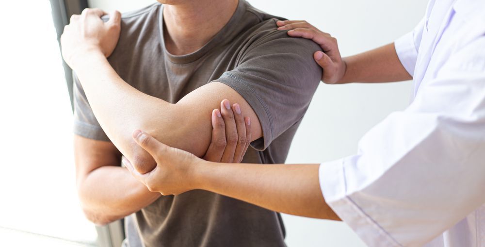 A Man Is Getting His Elbow Examined By A Doctor — Back In Motion Chiropractic & Healthcare In Innisfail, QLD