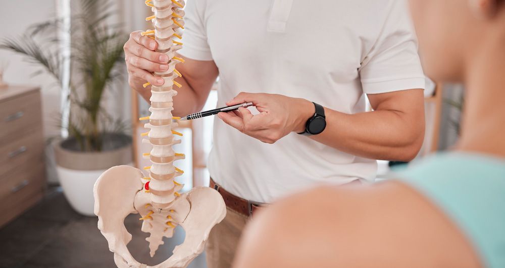 A Man Is Holding A Model Of A Spine And Talking To A Woman — Back In Motion Chiropractic & Healthcare In Mission Beach, QLD