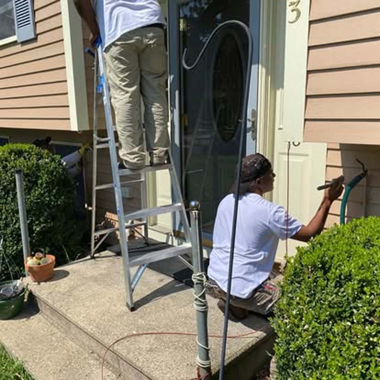 Two men are working on the front door of a house.