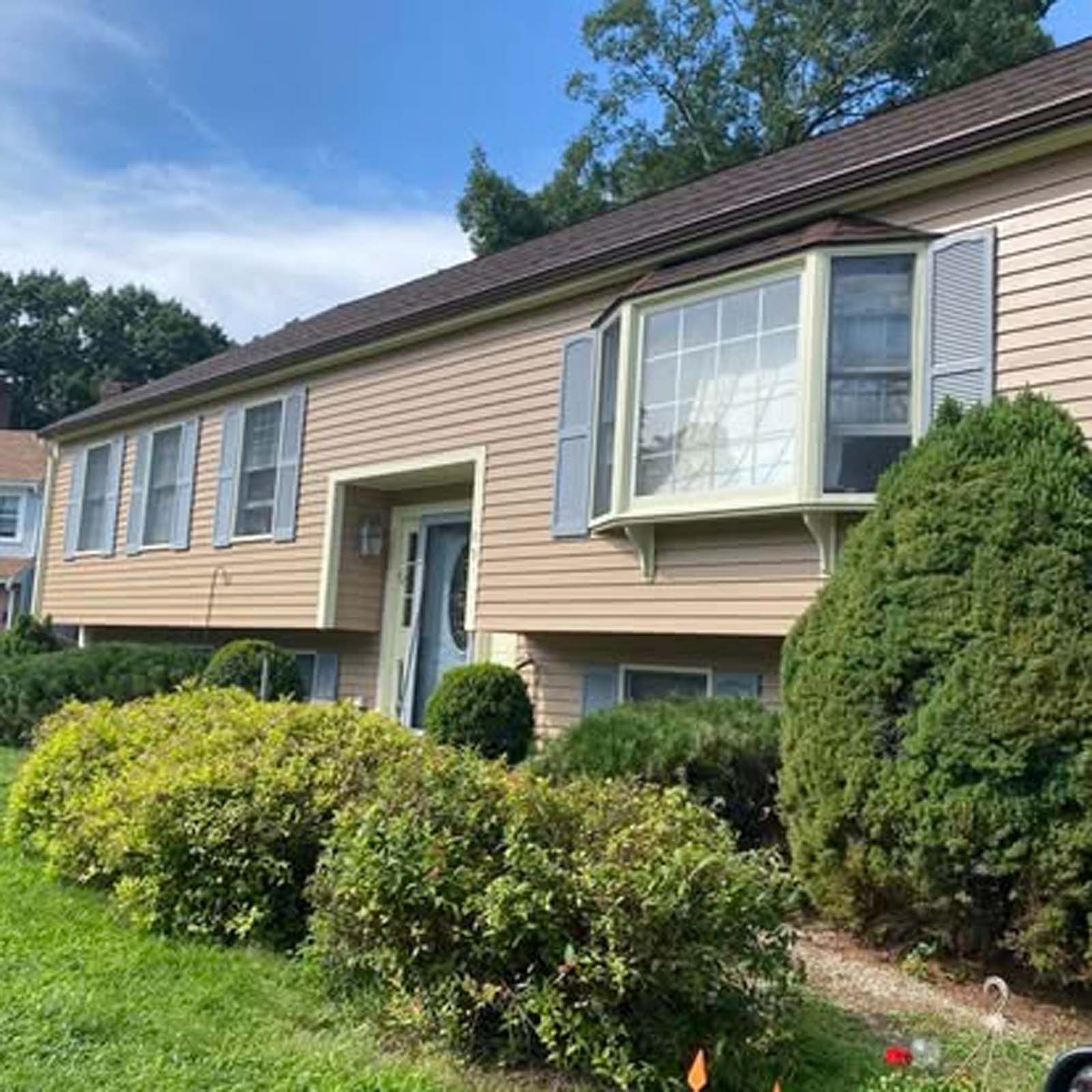A house with a large bay window is surrounded by bushes and trees.
